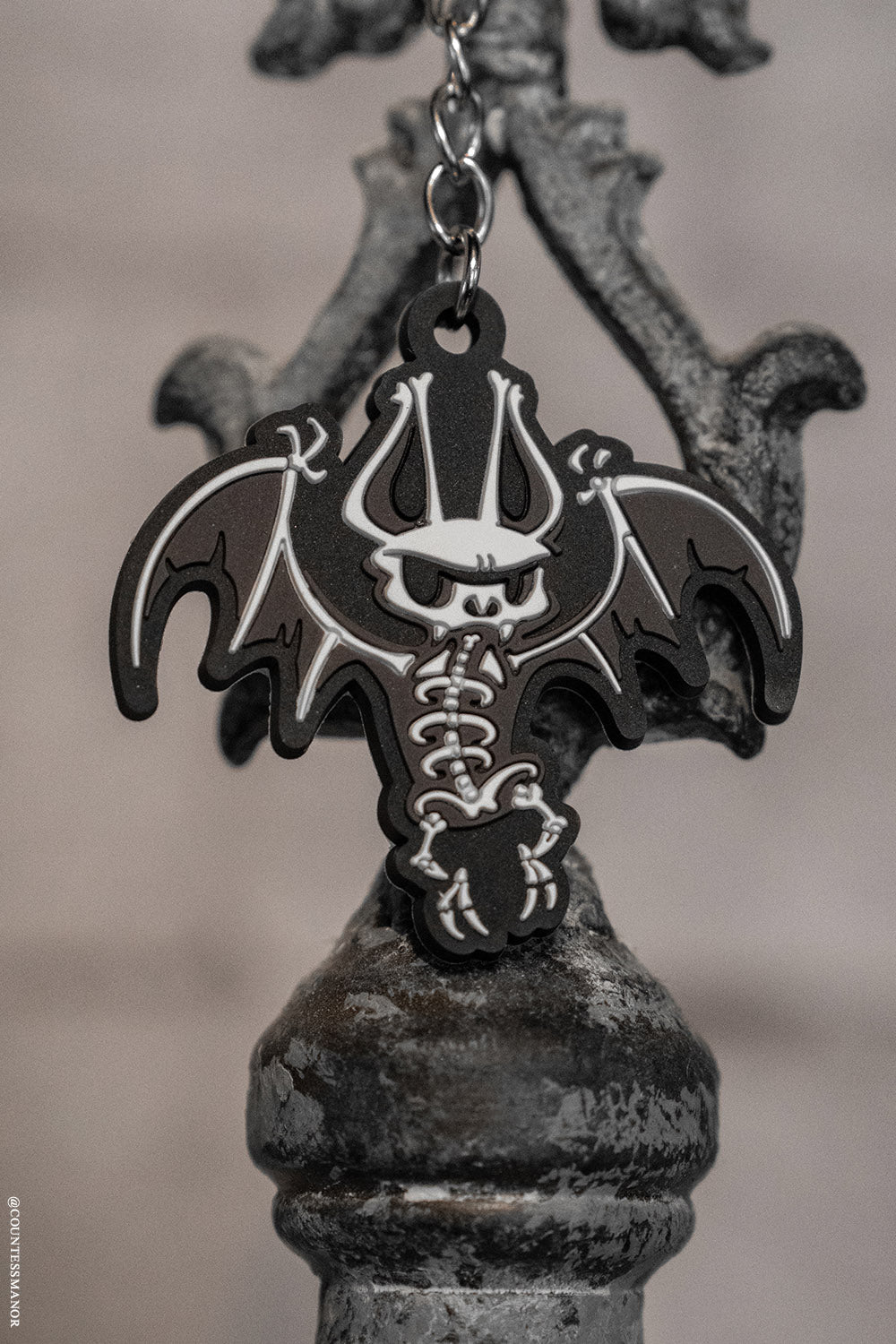 Bat-shaped keychain with skeleton design on a metallic stand against a blurred background