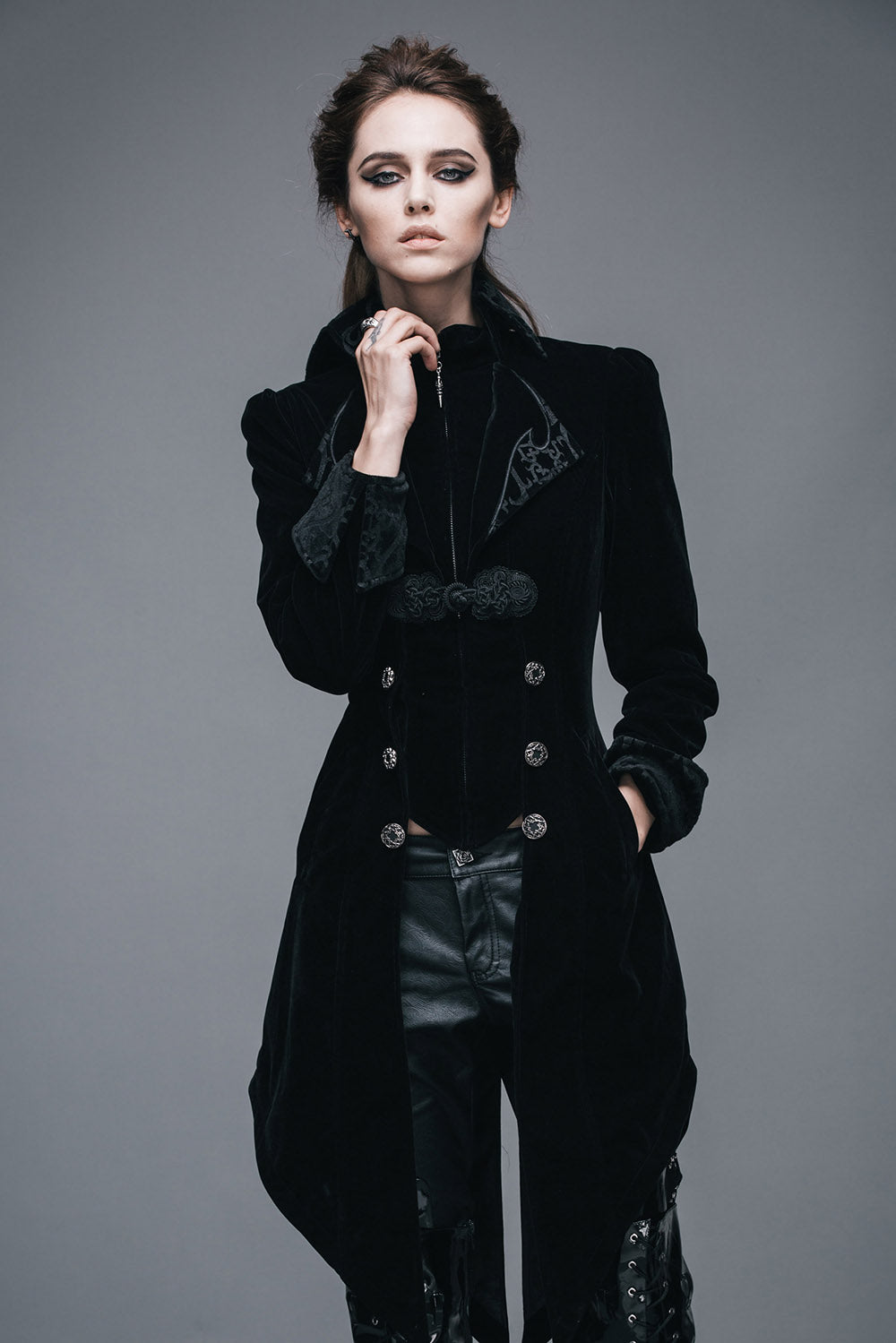 A woman wearing a black velvet gothic jacket with a vintage lapel, decorative buttons, and a swallowtail hem.