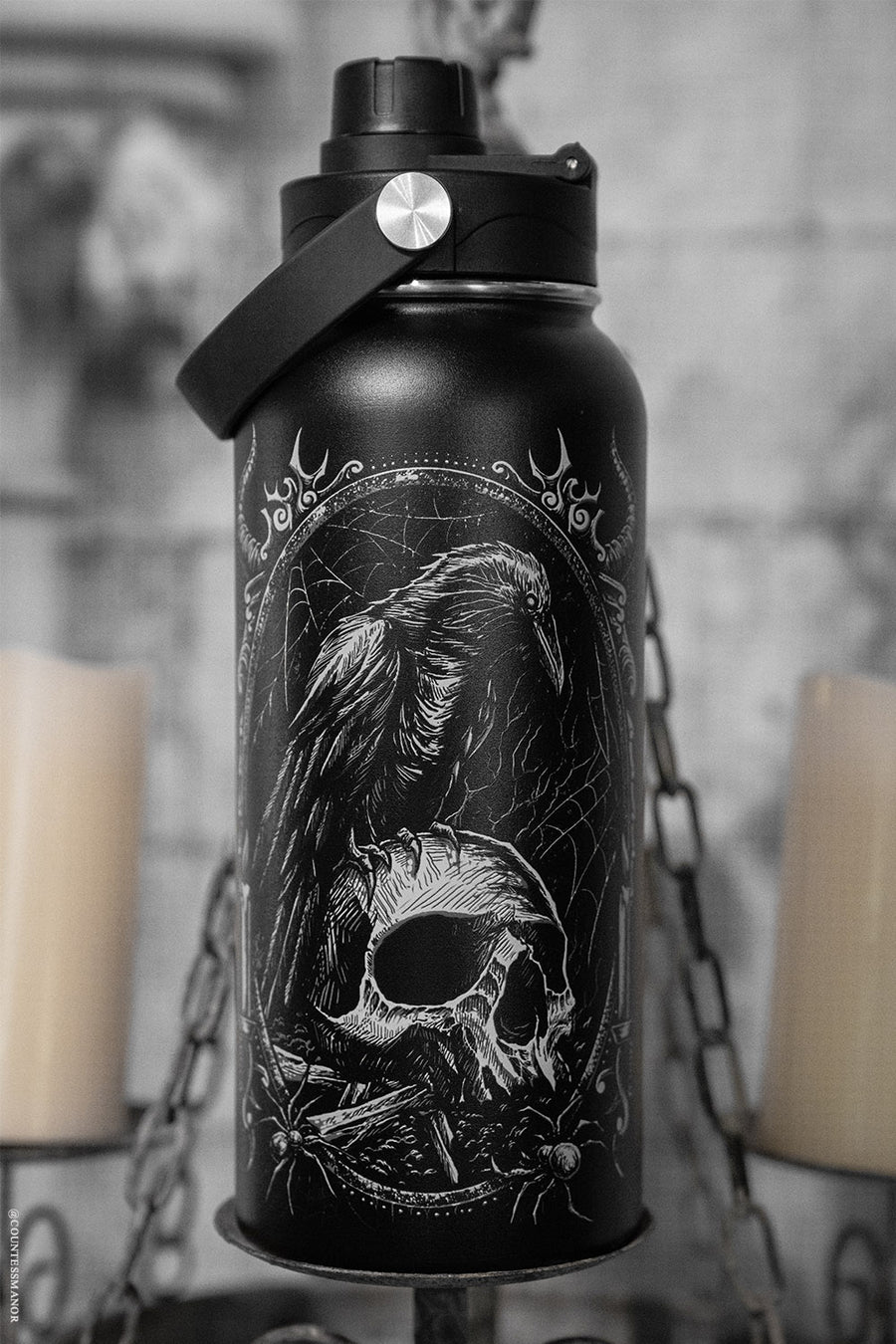 Black water bottle with skull and raven design against a gray background