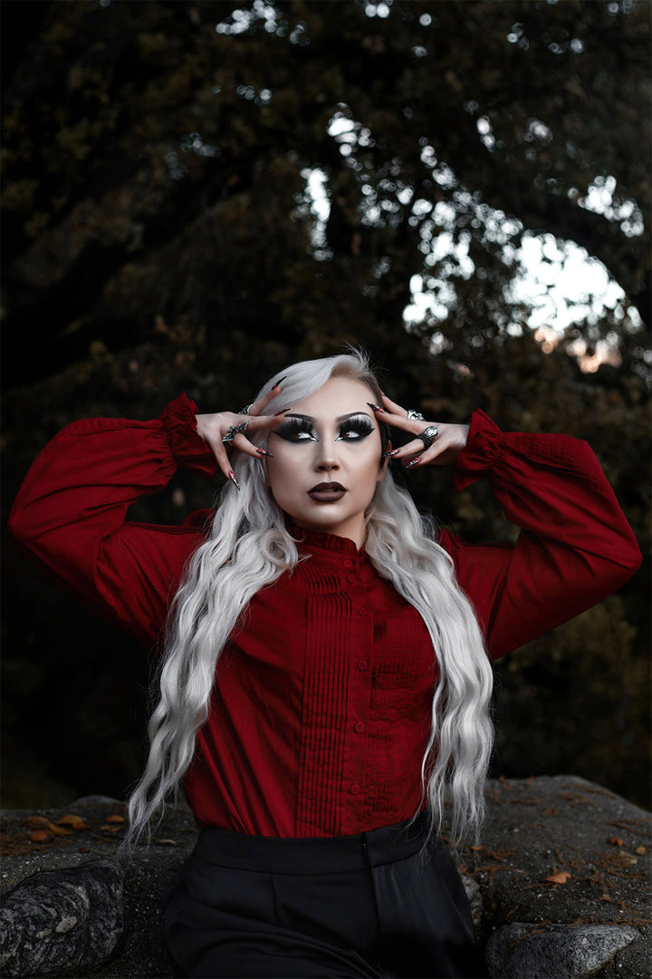 Person with long white hair wearing a red shirt in a forest setting