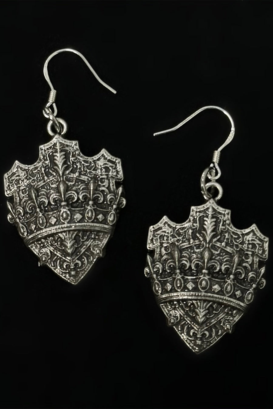 Silver shield-shaped earrings with intricate designs on a black background