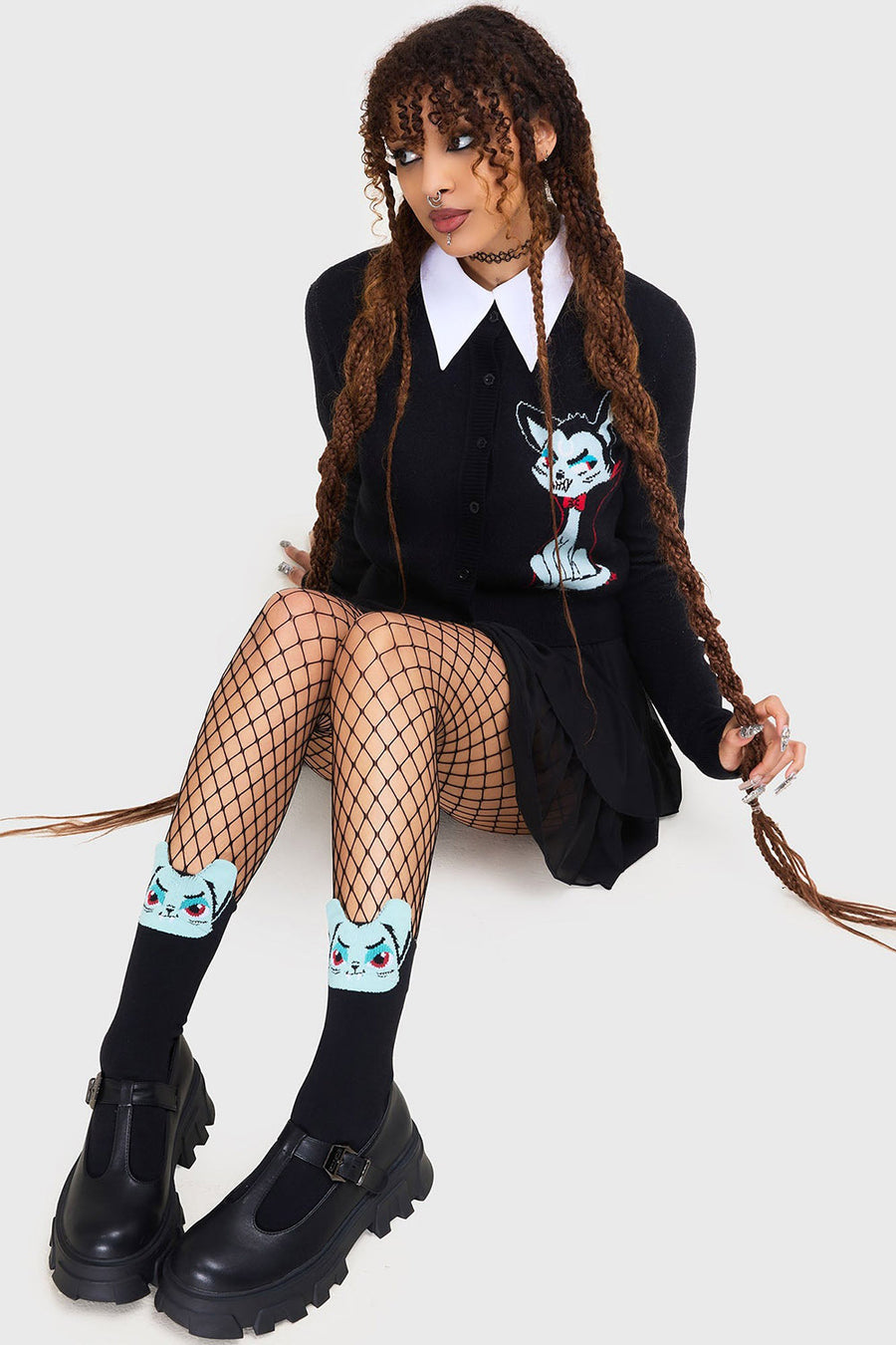 gothic girl wearing a black outfit with fishnet stockings, creepy cat socks, and black shoes on a white background
