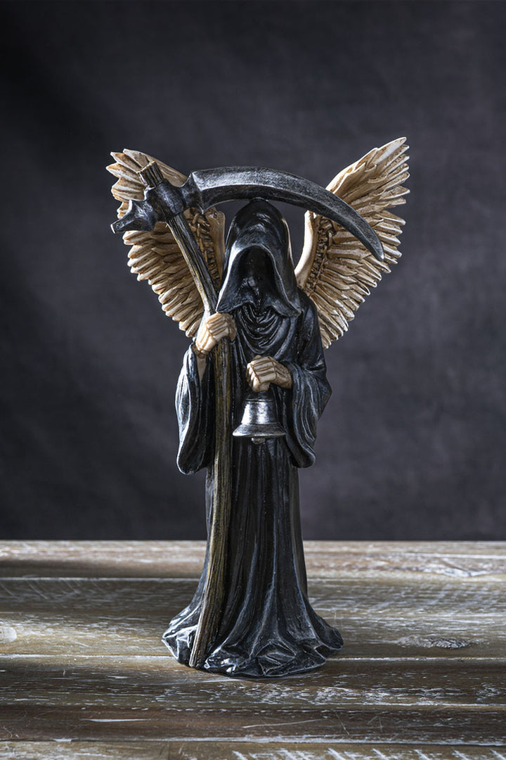 Statue of an angel with a scythe on a wooden surface with a dark background