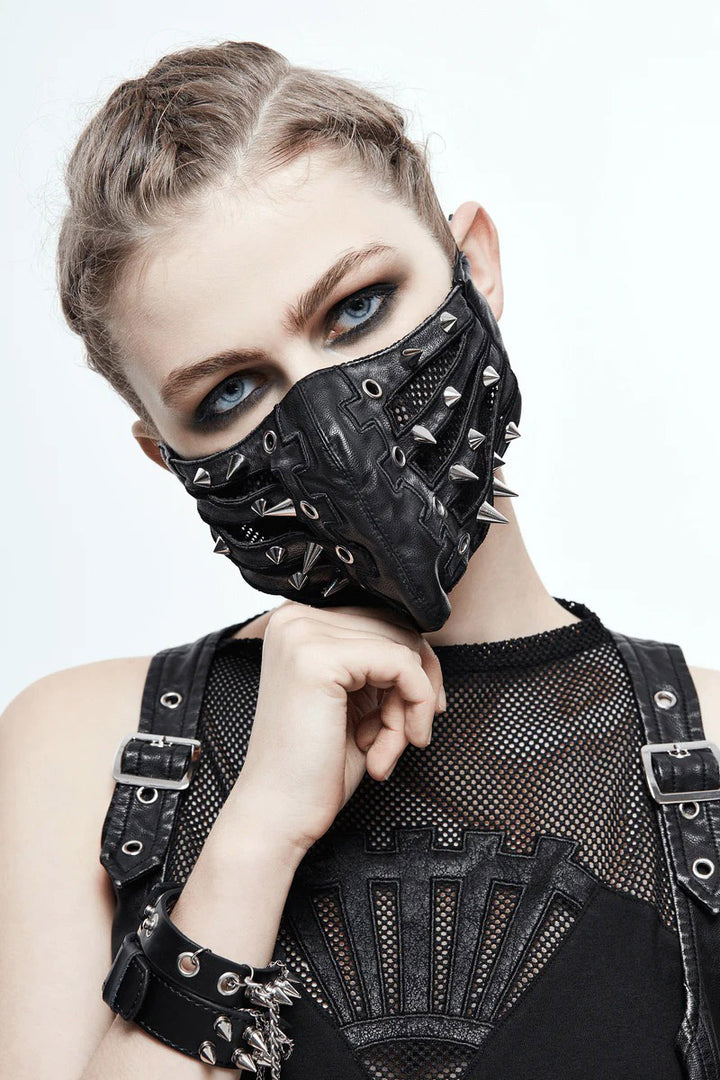 A person wearing a black unisex punk face mask with silver rivet spikes, metal eyelets, and black mesh netting. The mask has elastic ear loops and is made of vegan leather.