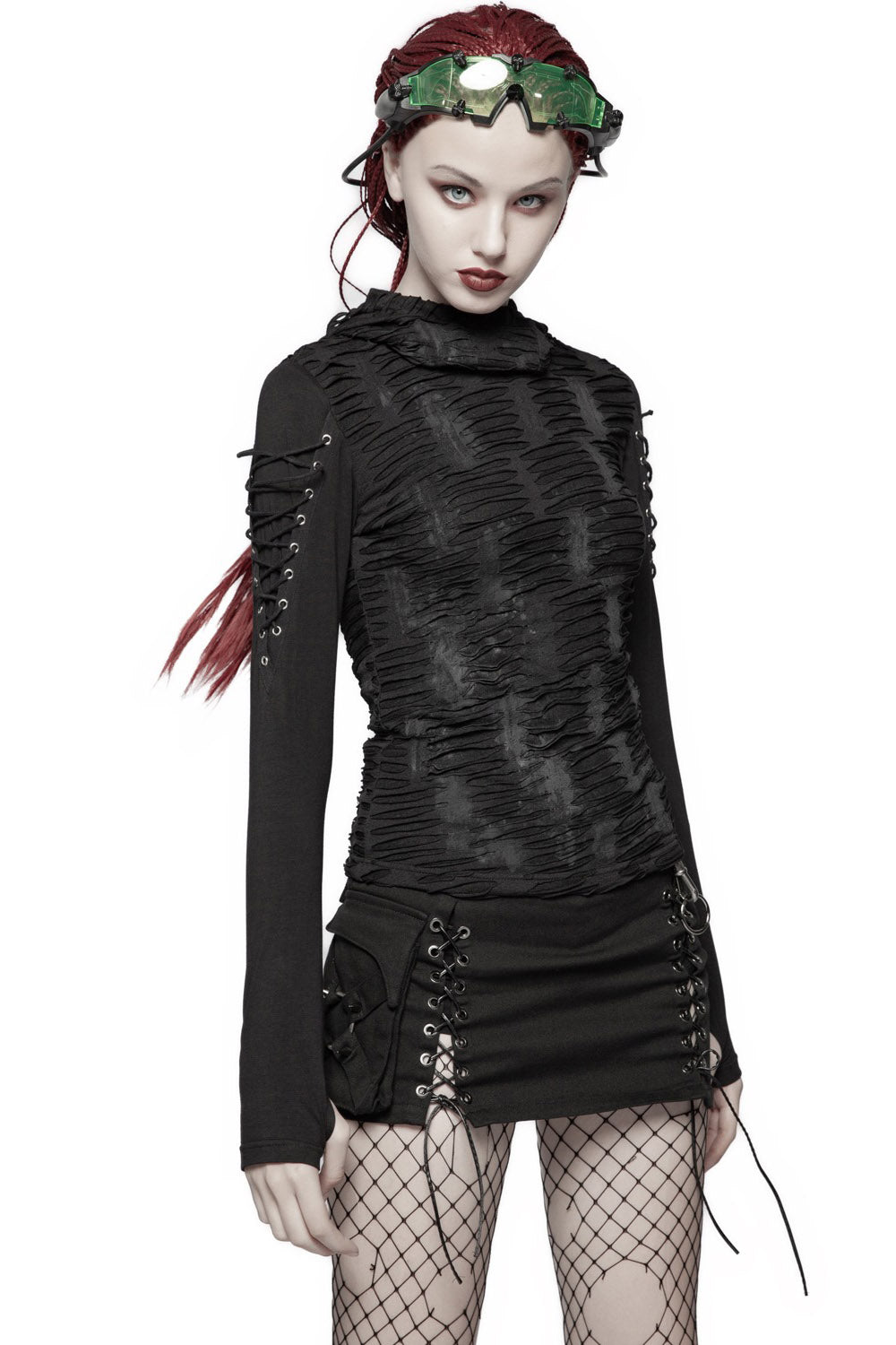 A woman wearing a black post-apocalyptic style hooded top with distressed details and silver eyelets. The top features attached hood, shoulder laces, thumbhole cutouts, and is made from woven knit fabric.