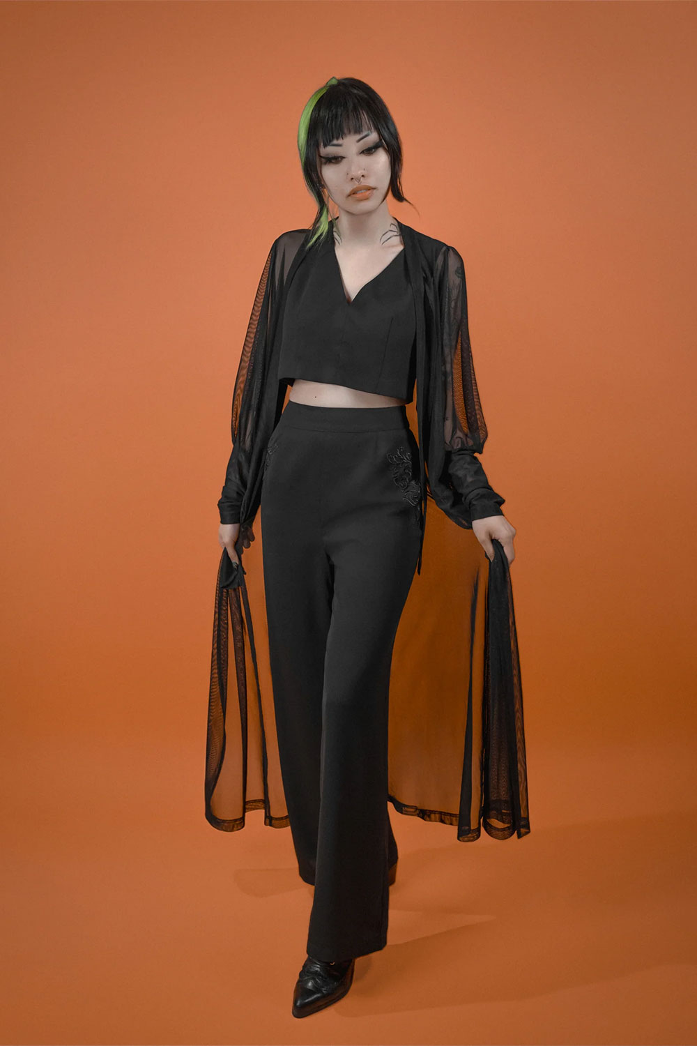 female model wearing Beyond the Veil Duster from Lively Ghosts over black top and black bottoms against orange background