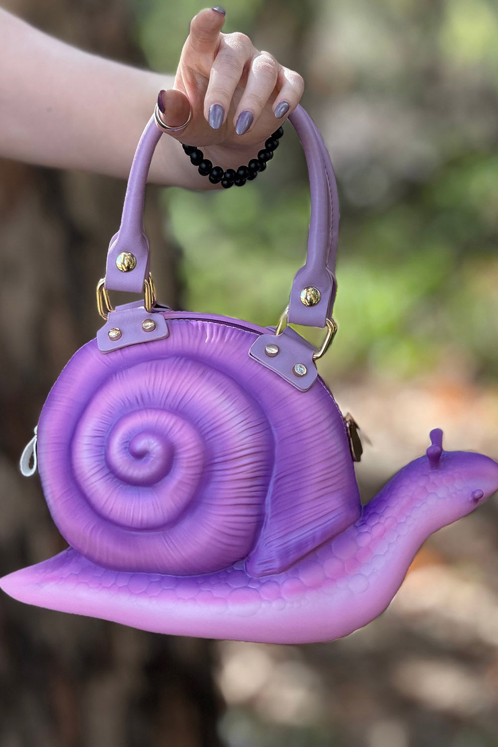 Purple snail-shaped handbag held by a person with a blurred natural background