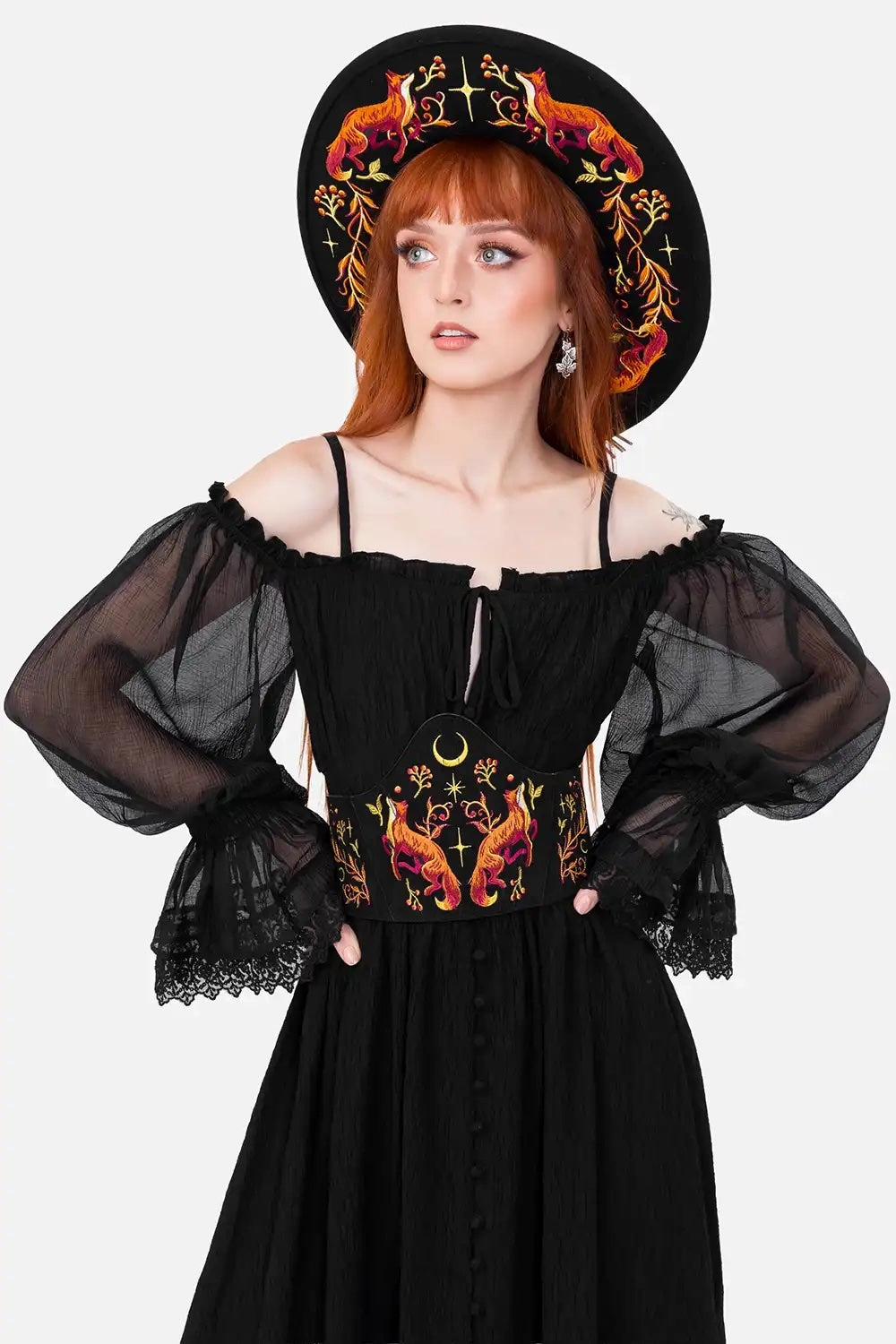 Woman wearing a black dress with floral embroidered corset and a matching hat on a white background