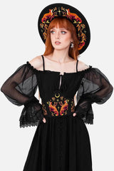 Woman wearing a black dress with floral embroidered corset and a matching hat on a white background