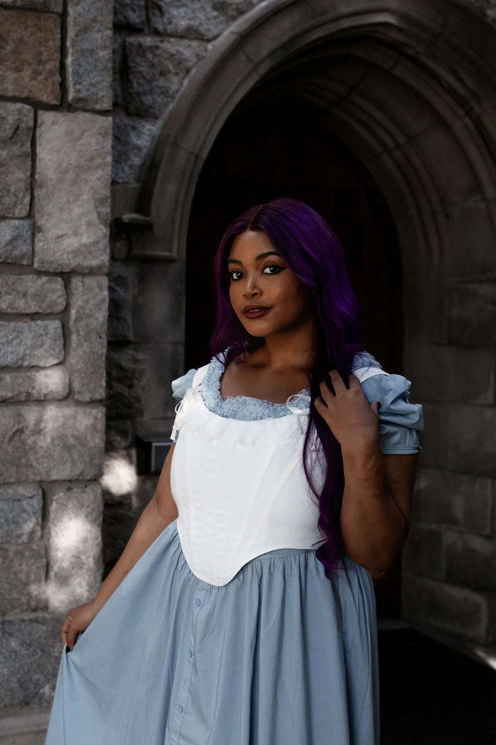 female model with purple hair wearing a light blue dress with a while corset