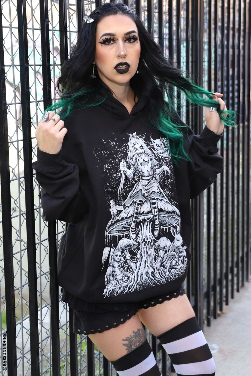 Person wearing a black hoodie with a white graphic design, standing against a metal fence.