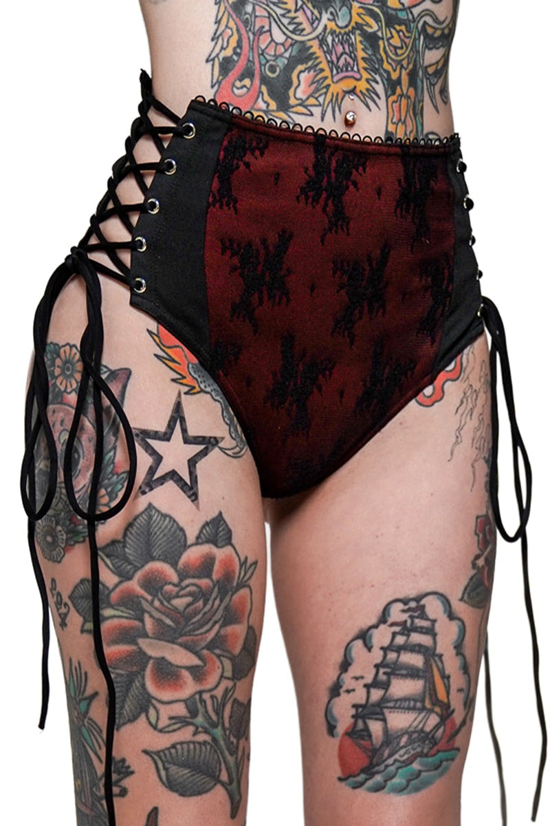 High-waisted red and black patterned bathing suit shorts with lace-up sides on a person with tattoos.
