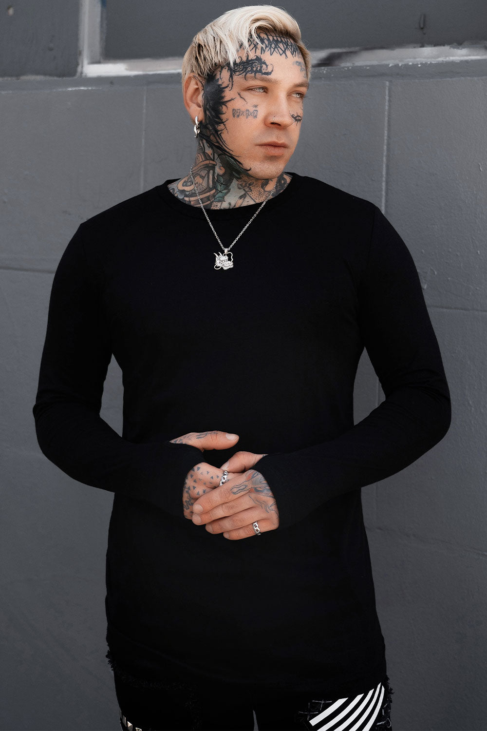 gothic man wearing a black long-sleeve shirt against a gray wall