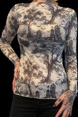 A long-sleeve mock-neck top with a gothic graveyard and forest print, featuring black trees, tombstones, and bats on an off-white background, modeled on a person against a black backdrop.