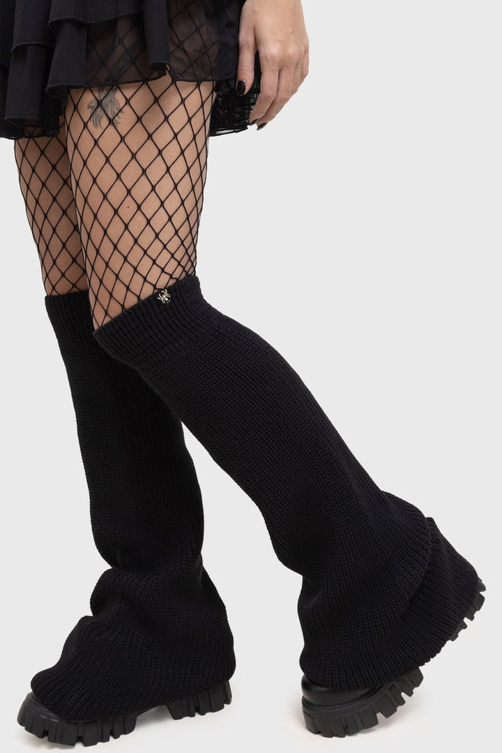 Black ribbed knee-high leg warmers worn with fishnet stockings on a white background