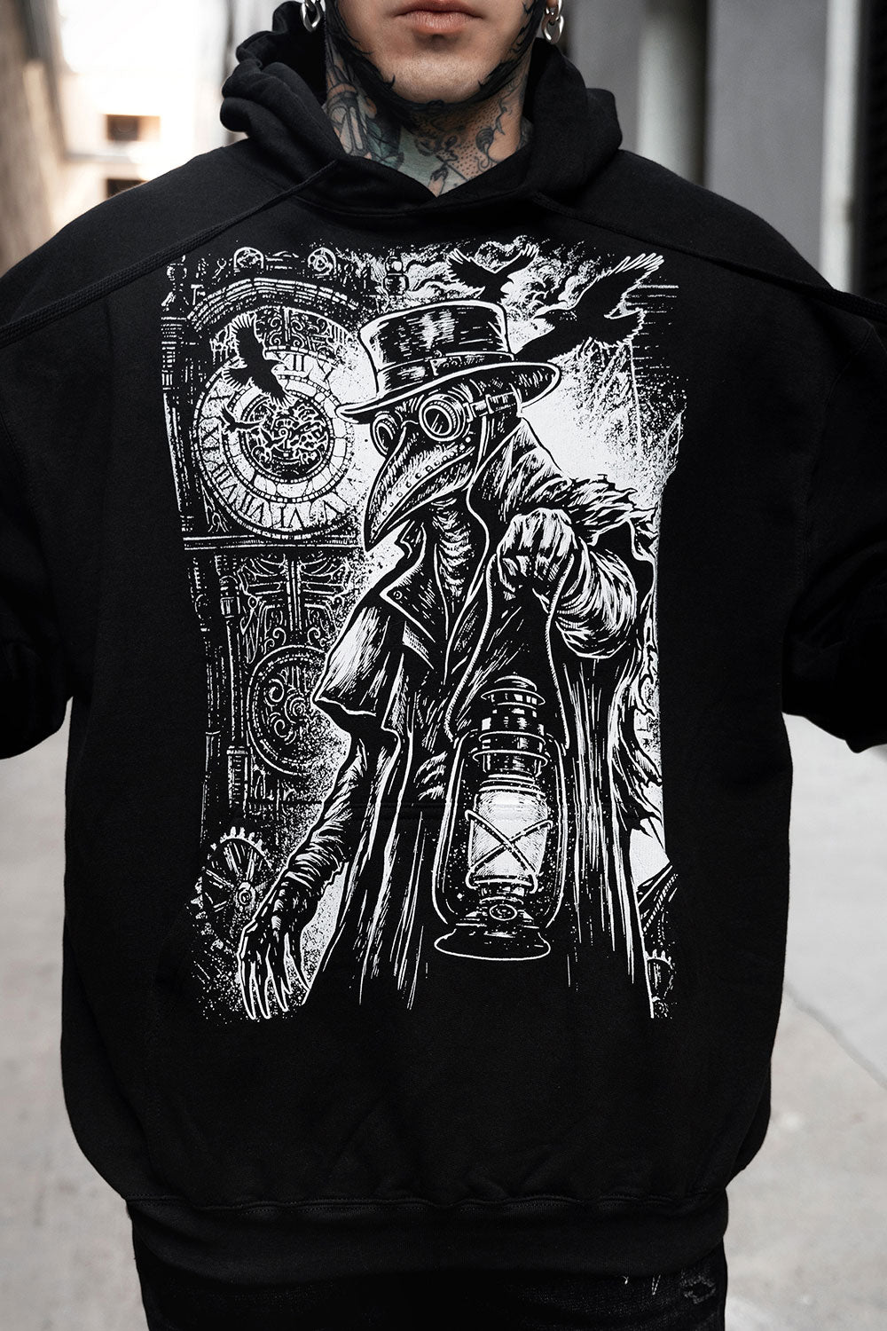 Black hoodie with intricate white graphic design of a plague doctor person in a coat and hat holding a lantern.