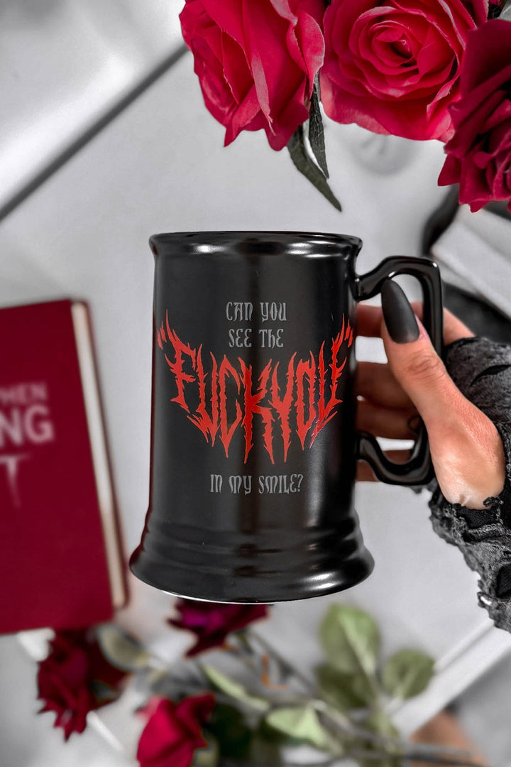 Black mug with red text held by a hand, surrounded by red roses and a book.