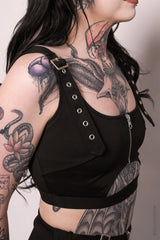 Person wearing a black crop top biki  with straps and buckles, showcasing tattoos on arms and neck.