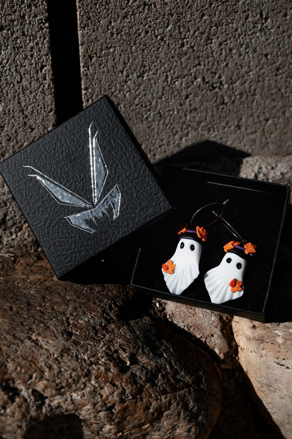 Halloween-themed ghost earrings in a black box on a textured surface