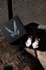 Halloween-themed ghost earrings in a black box on a textured surface