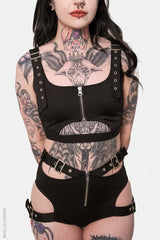 Person wearing a black harness outfit with visible tattoos on a white background