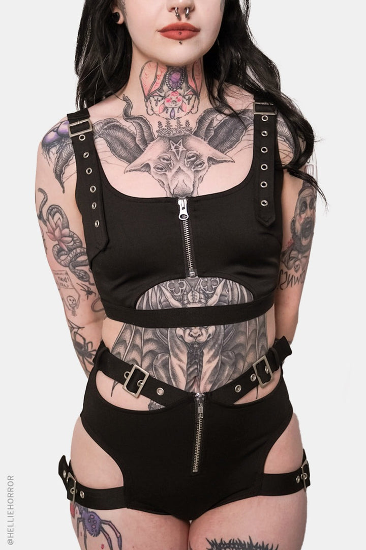 Person wearing a black harness outfit with visible tattoos on a white background