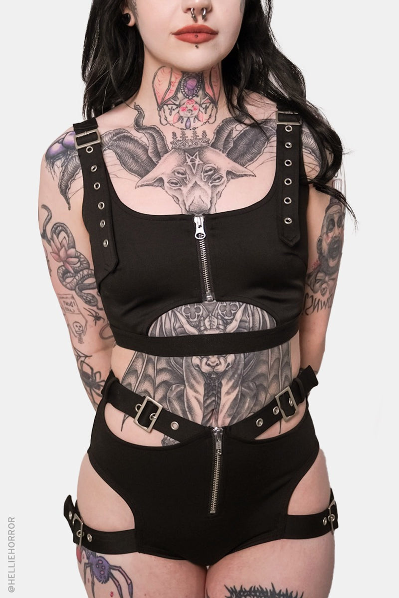 Person wearing a black harness outfit with visible tattoos on a white background