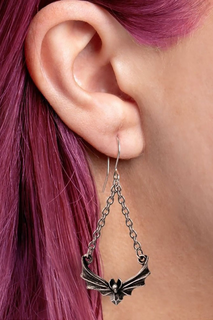 Close-up of an ear wearing a bat-shaped earring with pink hair.