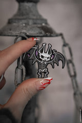 Hand holding a black and white skeleton bat pin against a blurred background