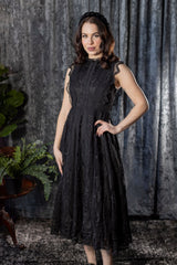 Woman wearing a black lace dress against a textured gray curtain background