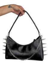 Black handbag with spikes and chain detail held by a hand on a white background