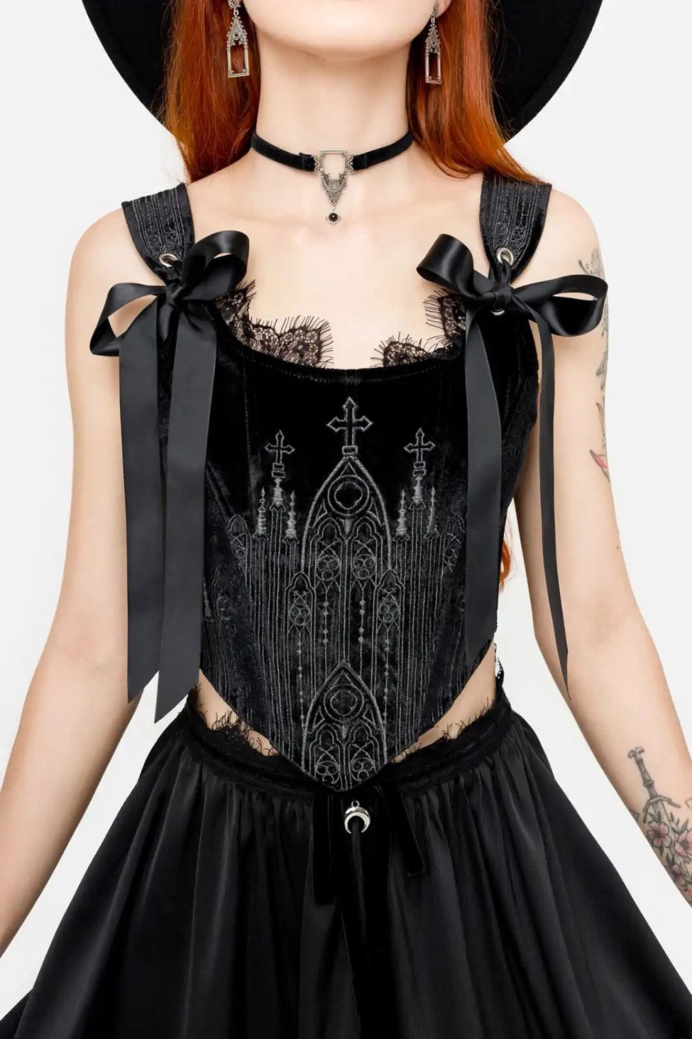 Person wearing a black corset with intricate designs and bows on a white background