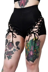 Black lace-up shorts worn by a person with tattoos on a white background