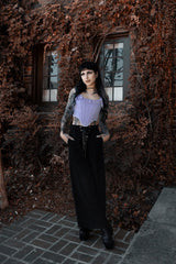 Woman in a gothic outfit including a gothic corset standing in front of an ivy-covered wall.