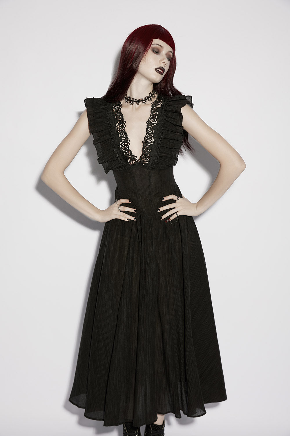 Woman wearing a black dress with ruffled sleeves and lace details on a white background