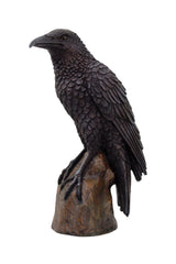 Black crow figurine on a wooden perch against a white background