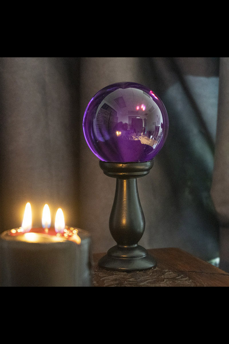 Purple glass orb on a stand with candles in the background