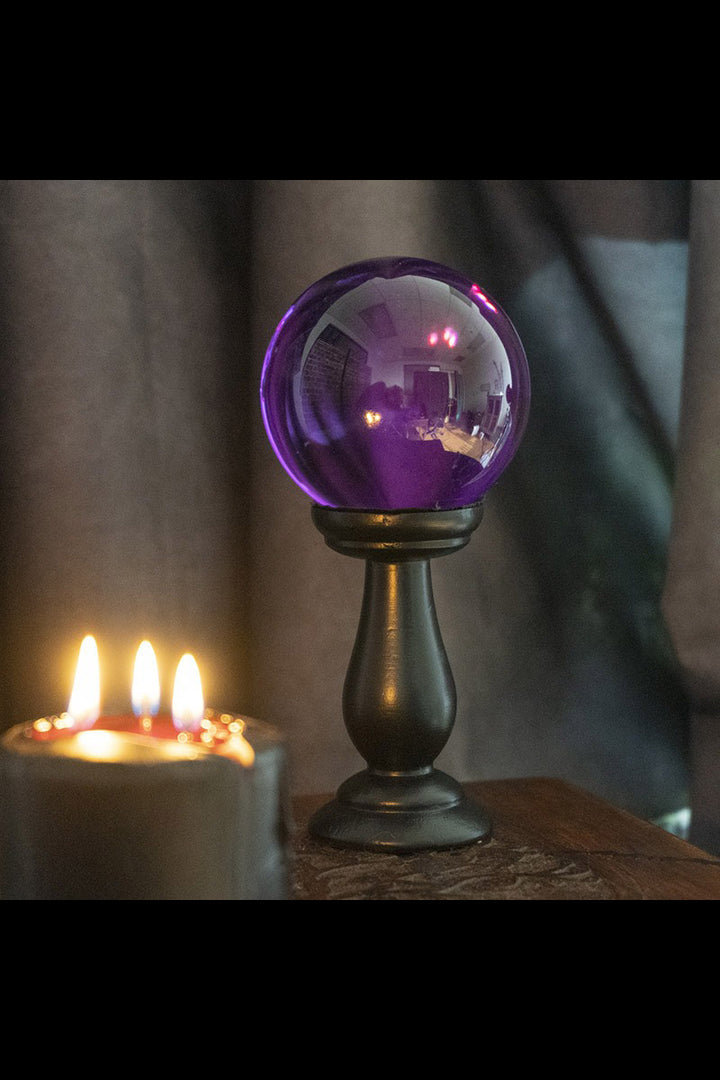 Purple glass orb on a stand with candles in the background