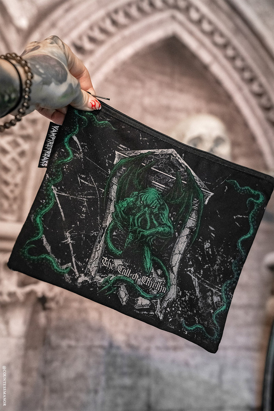 Black pouch with green and white Cthulhu design held by a hand against an architectural background