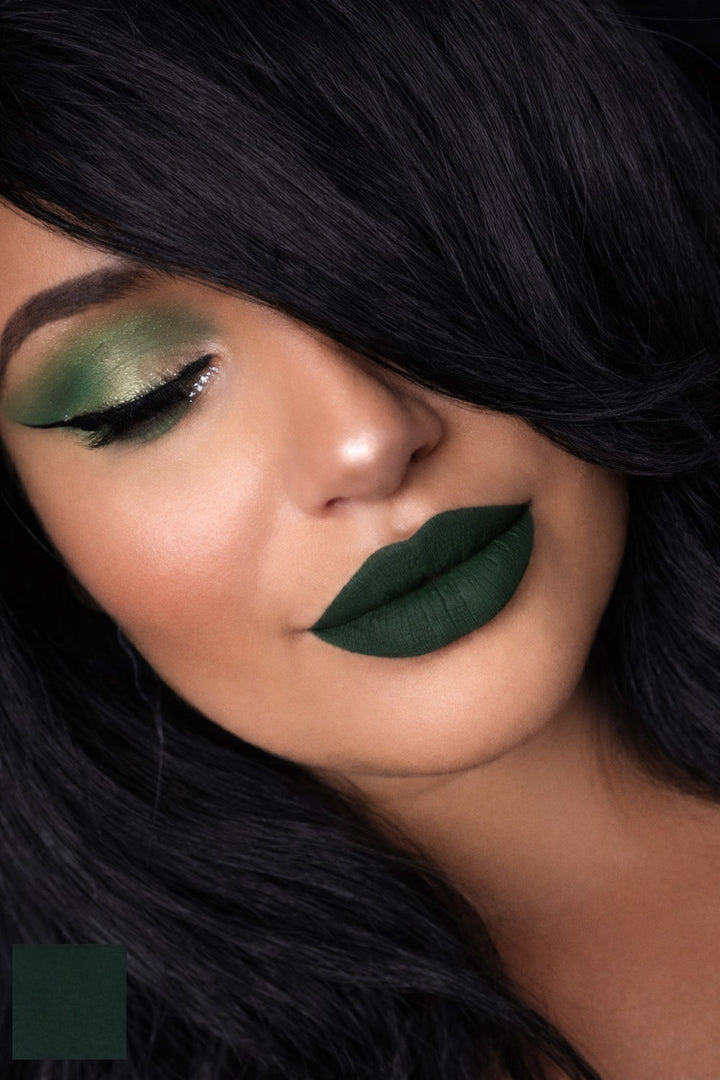 Close-up of a person with green eyeshadow and lipstick, wearing a black wig.