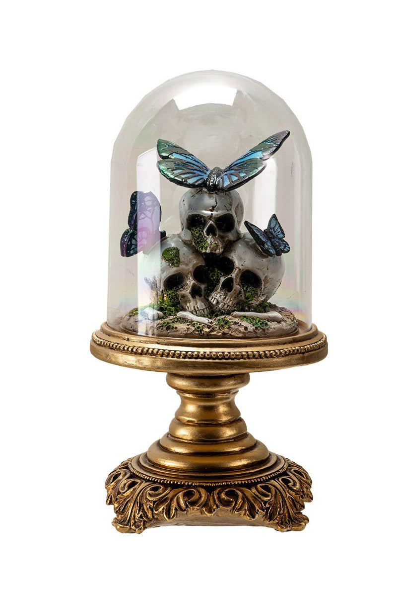 Decorative display with skull, butterflies, and bones under a glass dome on an ornate brass stand.