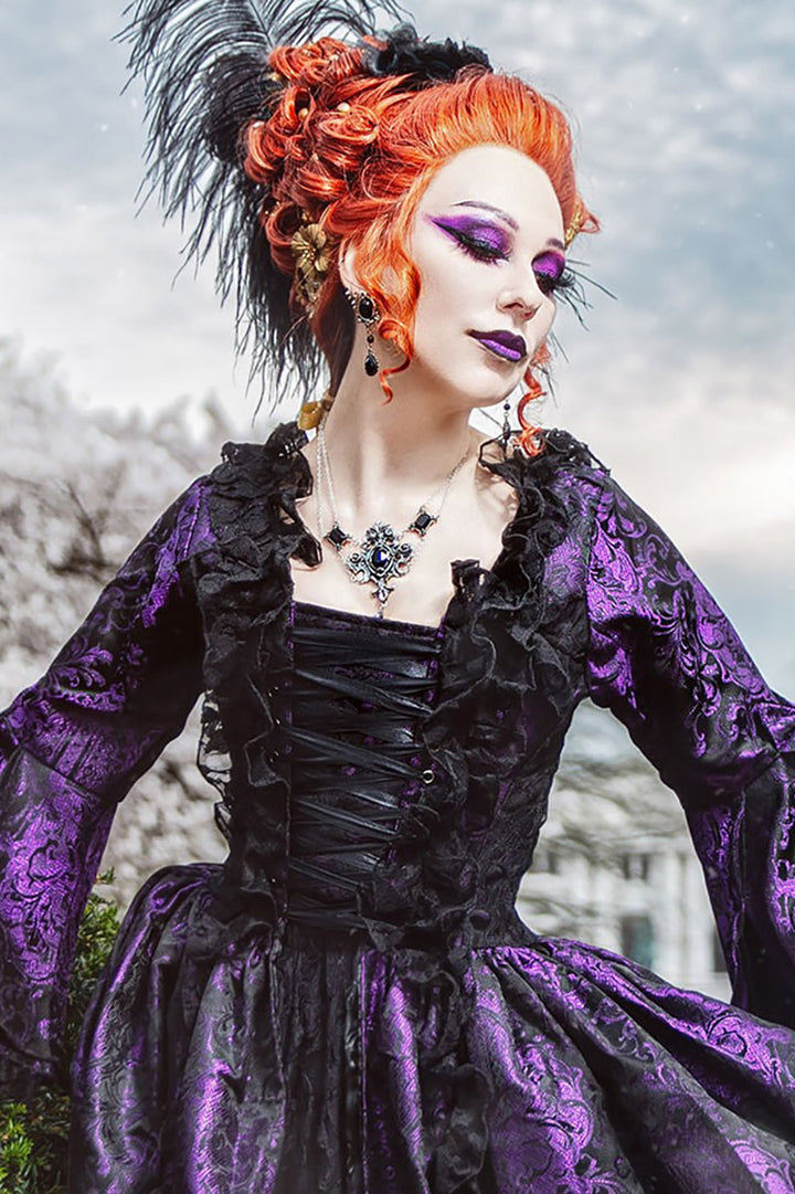 Person in a purple and black gothic-style dress with orange hair and feathered headpiece wearing goth necklace