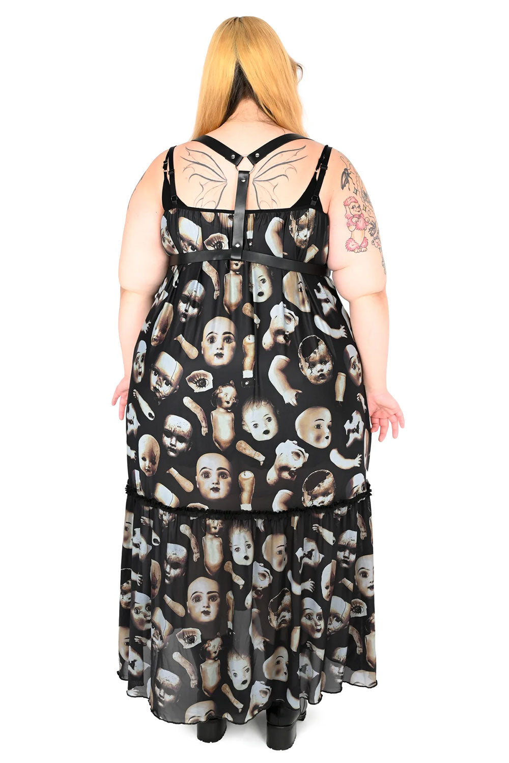 Back view of model wearing a long black dress with broken doll parts on the fabric
