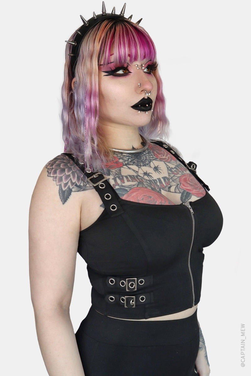 Person with tattoos wearing a black outfit with shoulder straps on a white background