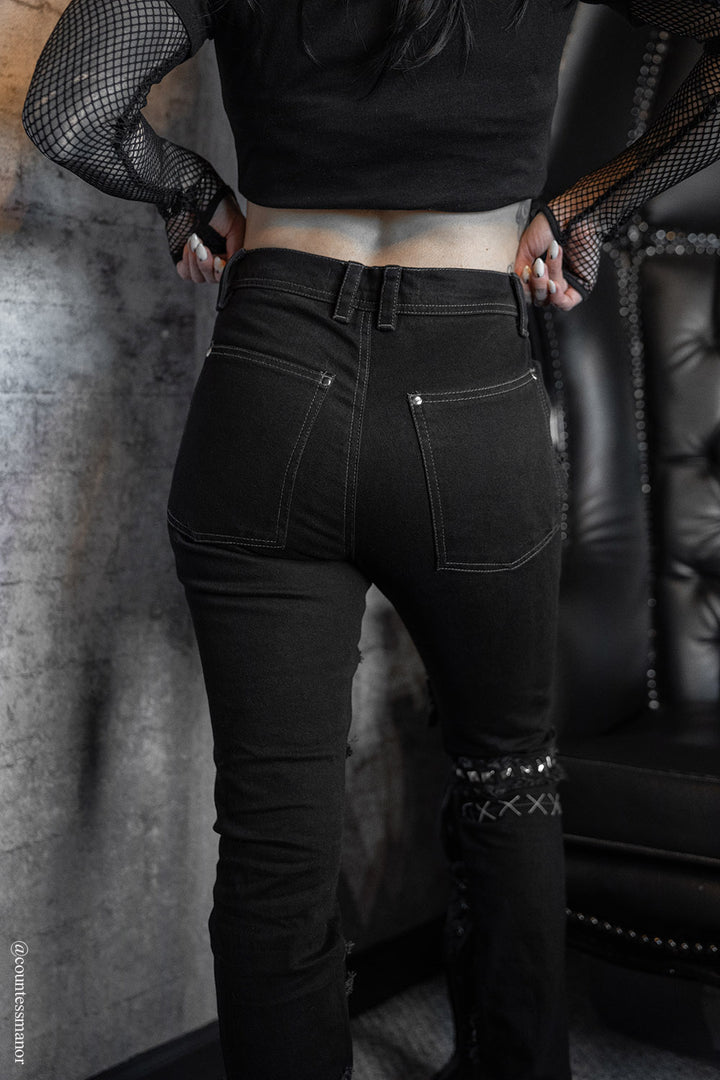 gothic skinny jeans with shredded details, distressing, a striped patch, and a skull patch