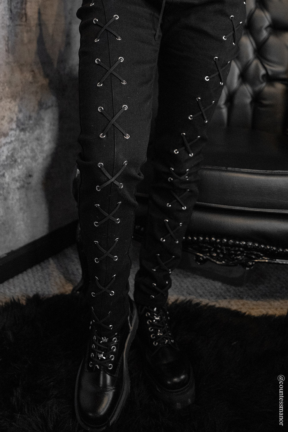 Black lace-up boots worn with womens skinny jean pants against a textured wall.