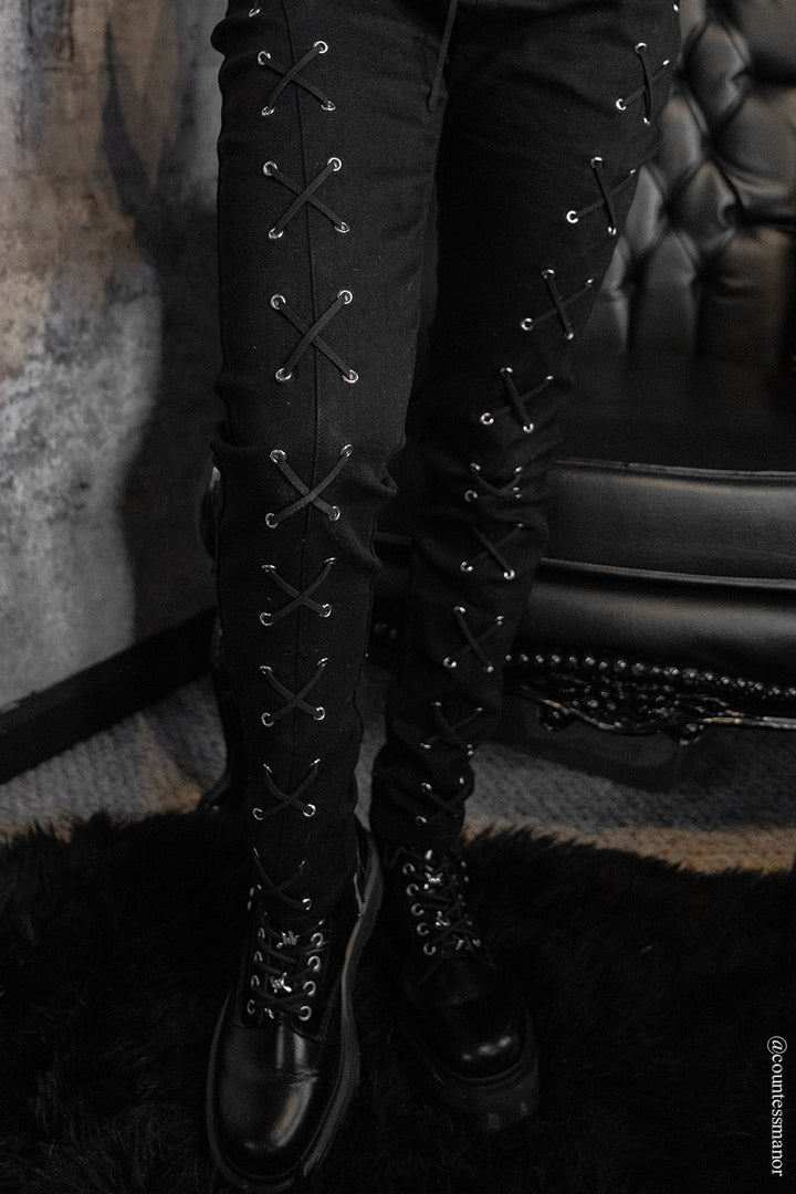 Black lace-up boots worn with womens skinny jean pants against a textured wall.