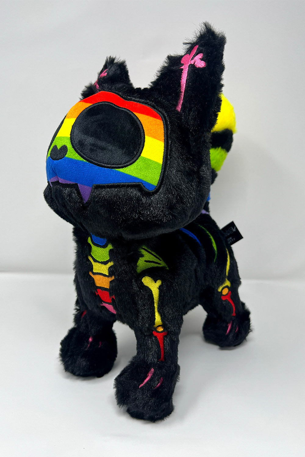 Black plush toy cat with rainbow accents on a white background