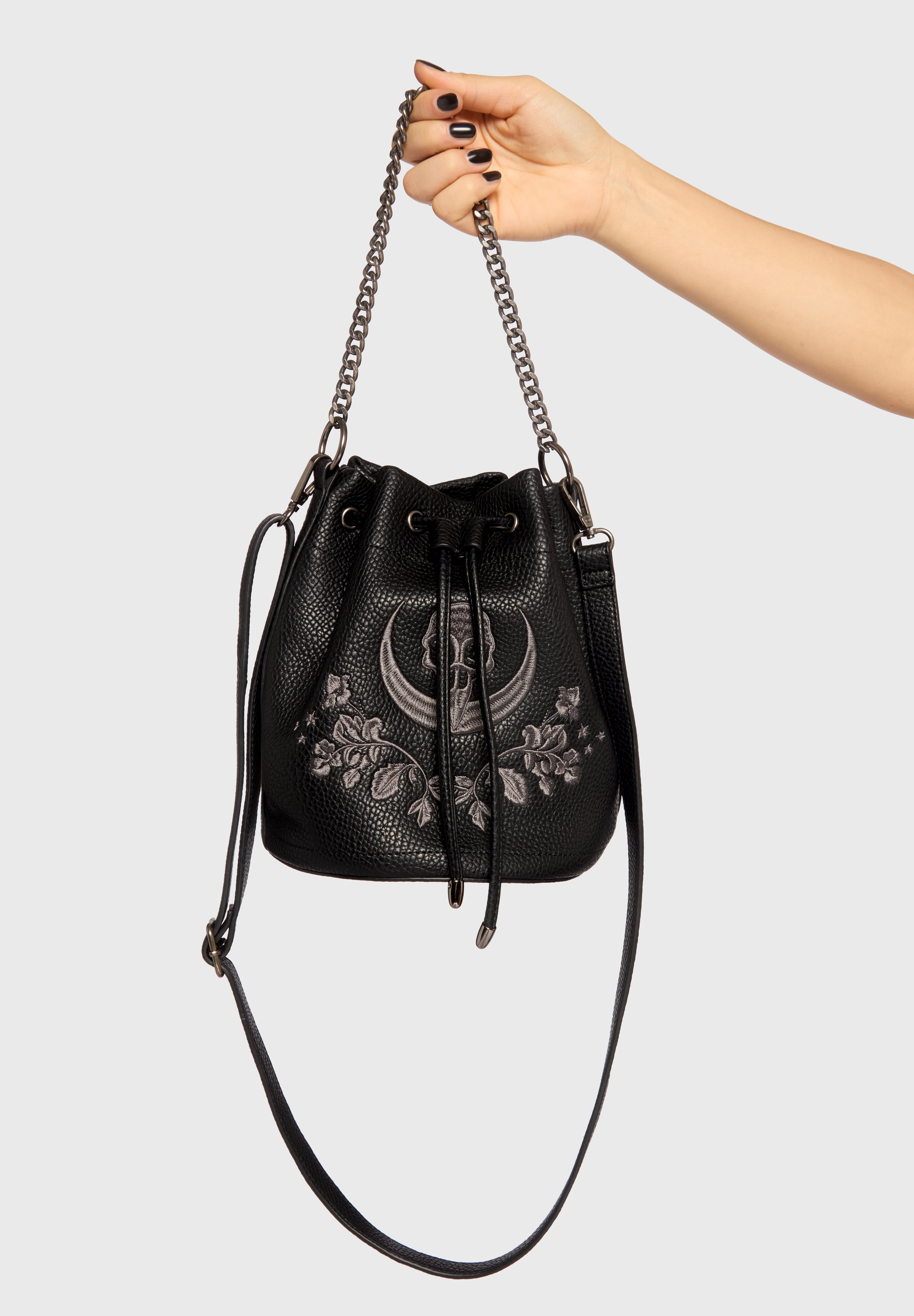 Black handbag with floral embroidery and chain strap held by a hand on a light gray background