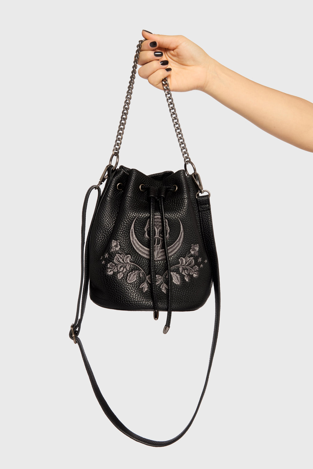 Black handbag with floral embroidery and chain strap held by a hand on a light gray background